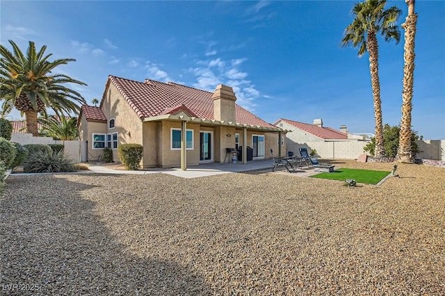 rear view of house featuring a patio, fence, a chimney, stucco siding, and a tiled roof