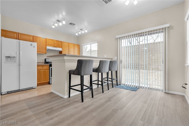 kitchen featuring rail lighting, a breakfast bar, light hardwood / wood-style floors, white fridge with ice dispenser, and stainless steel electric stove