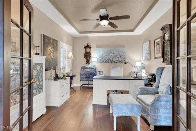 office featuring wood-type flooring, ceiling fan, and a tray ceiling