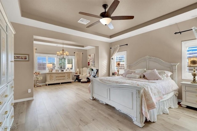 bedroom with ceiling fan with notable chandelier, light hardwood / wood-style floors, and a raised ceiling