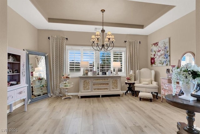 living area with a notable chandelier, light hardwood / wood-style floors, and a raised ceiling