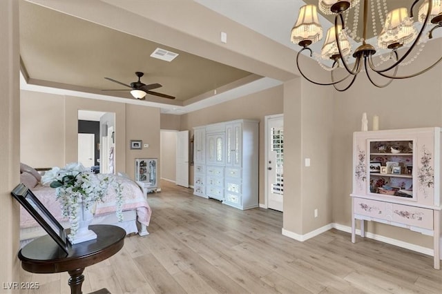 foyer featuring ceiling fan with notable chandelier, light wood-type flooring, and a tray ceiling