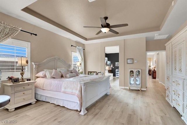 bedroom with ceiling fan, a tray ceiling, and light wood-type flooring