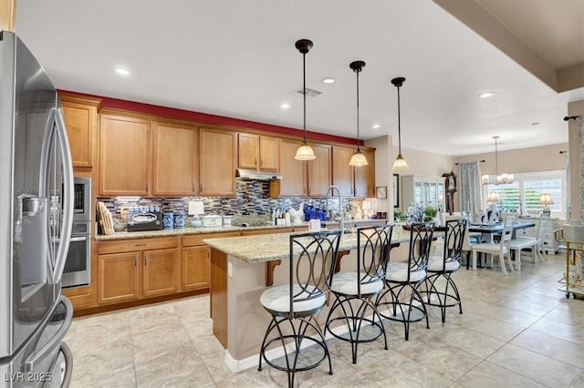 kitchen with stainless steel appliances, hanging light fixtures, a center island with sink, and a kitchen bar