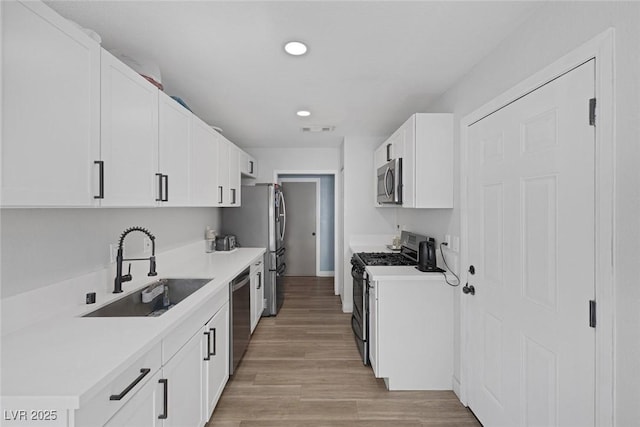 kitchen featuring stainless steel appliances, sink, light hardwood / wood-style flooring, and white cabinets