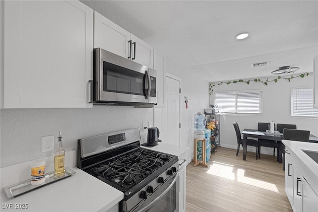 kitchen with stainless steel appliances, light hardwood / wood-style flooring, and white cabinets