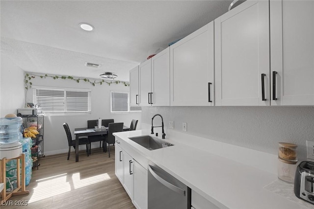 kitchen featuring white cabinetry, sink, stainless steel dishwasher, and light wood-type flooring