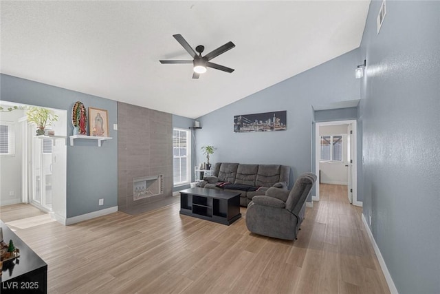 living room featuring a tiled fireplace, light hardwood / wood-style flooring, ceiling fan, and vaulted ceiling