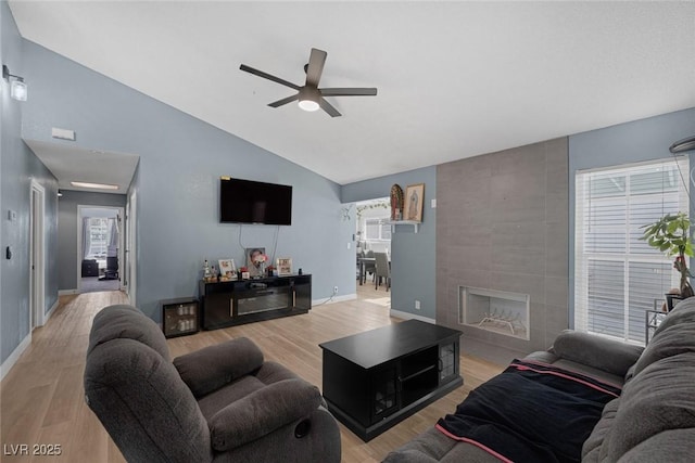 living room with a tile fireplace, lofted ceiling, ceiling fan, and light hardwood / wood-style flooring