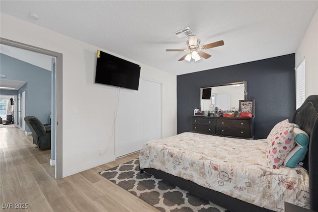 bedroom featuring ceiling fan, a textured ceiling, light wood-type flooring, and a closet