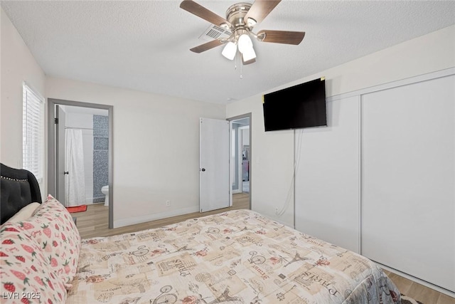 bedroom featuring ensuite bath, a textured ceiling, light wood-type flooring, a closet, and ceiling fan