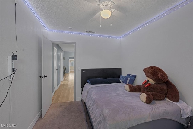 bedroom with ceiling fan, light colored carpet, and a textured ceiling