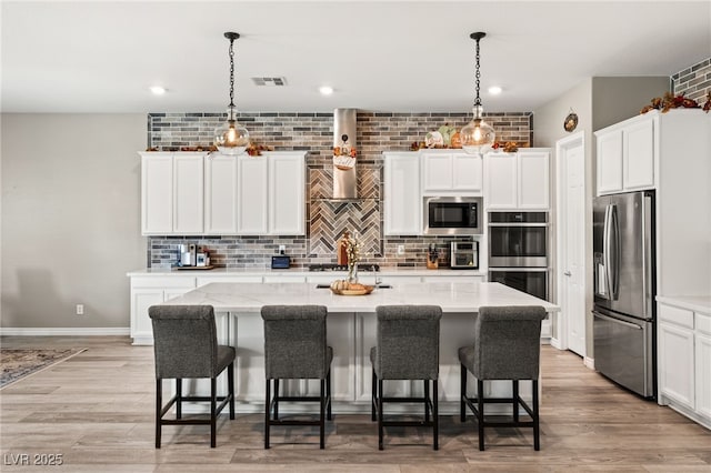 kitchen with stainless steel appliances, a kitchen island with sink, pendant lighting, and white cabinets