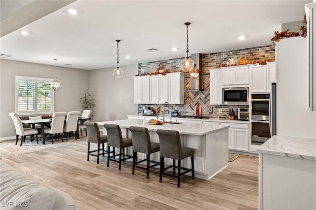 kitchen with pendant lighting, white cabinetry, stainless steel appliances, light stone counters, and an island with sink