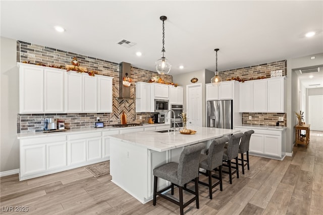 kitchen featuring hanging light fixtures, stainless steel appliances, an island with sink, white cabinets, and light wood-type flooring