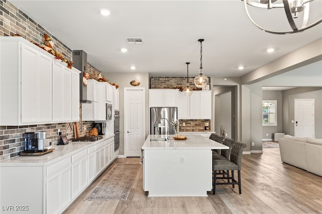 kitchen with a kitchen island with sink, pendant lighting, white cabinetry, and appliances with stainless steel finishes