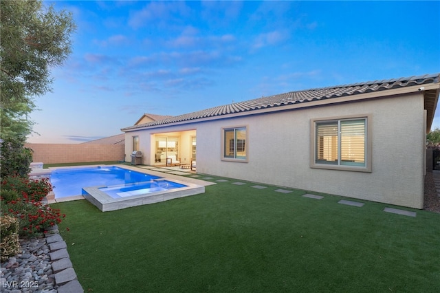 back house at dusk with a yard and a pool with hot tub