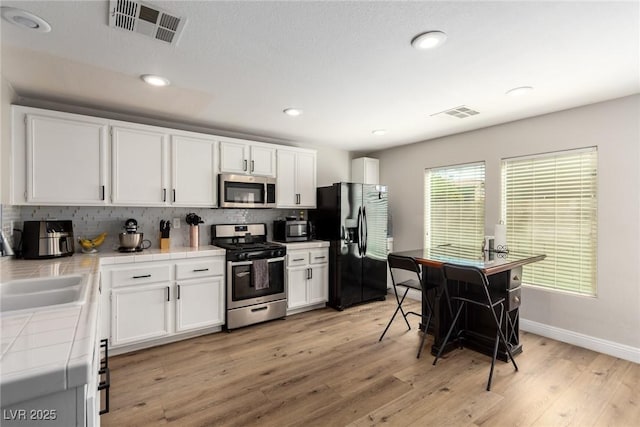 kitchen featuring sink, white cabinetry, appliances with stainless steel finishes, tile counters, and light hardwood / wood-style floors