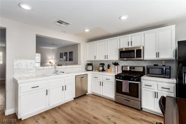 kitchen featuring sink, white cabinetry, light wood-type flooring, tile counters, and stainless steel appliances