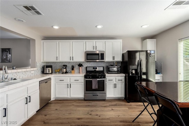 kitchen with sink, white cabinets, stainless steel appliances, light hardwood / wood-style floors, and backsplash