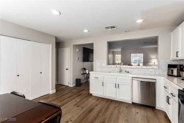 kitchen featuring sink, dishwasher, light hardwood / wood-style floors, white cabinets, and decorative backsplash