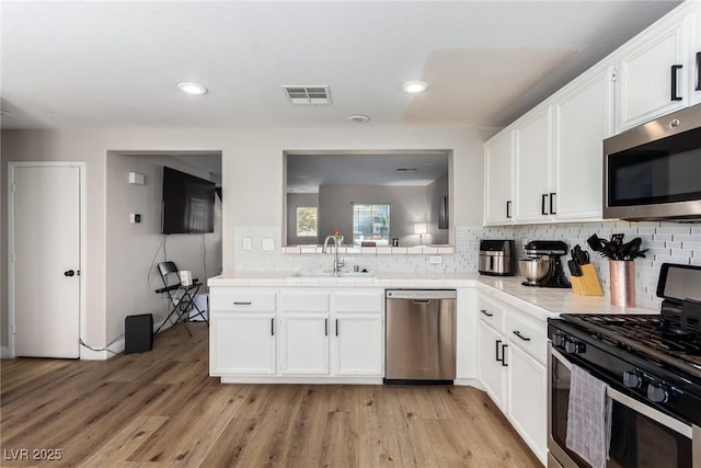 kitchen featuring sink, light hardwood / wood-style flooring, white cabinetry, stainless steel appliances, and tasteful backsplash