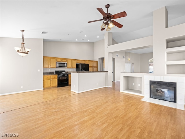 kitchen with light hardwood / wood-style flooring, a tile fireplace, pendant lighting, ceiling fan, and black appliances