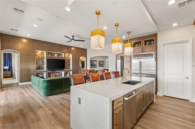 kitchen with sink, light stone counters, decorative light fixtures, a center island with sink, and light hardwood / wood-style floors