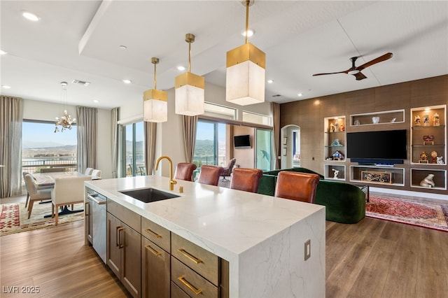 kitchen with sink, light stone countertops, light hardwood / wood-style floors, a center island with sink, and decorative light fixtures