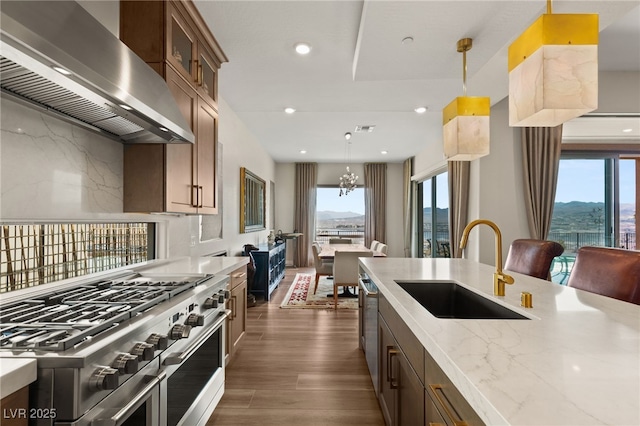 kitchen with double oven range, decorative light fixtures, range hood, and sink