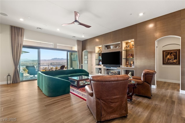 living room with wood-type flooring, ceiling fan, and built in shelves