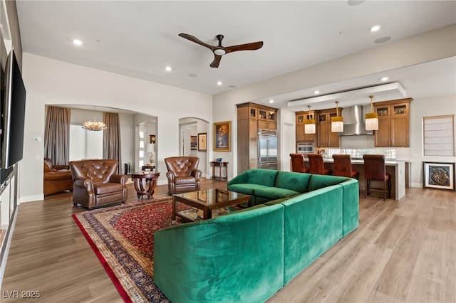 living room featuring ceiling fan with notable chandelier and light wood-type flooring