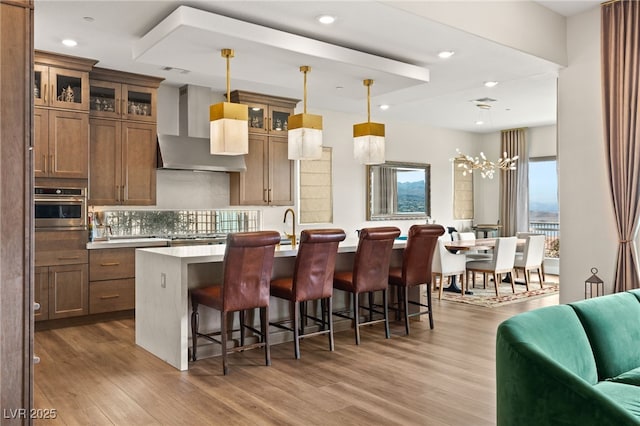 kitchen with pendant lighting, wall chimney range hood, a center island with sink, a kitchen bar, and stainless steel oven