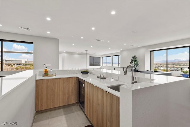 kitchen featuring visible vents, modern cabinets, brown cabinets, a peninsula, and a sink