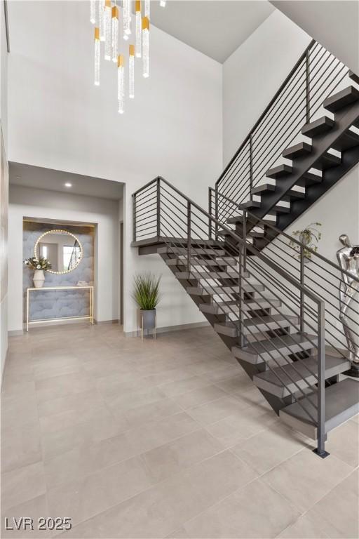 stairs with a towering ceiling, an inviting chandelier, and baseboards