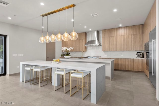 kitchen featuring wall chimney range hood, modern cabinets, light countertops, and a large island with sink