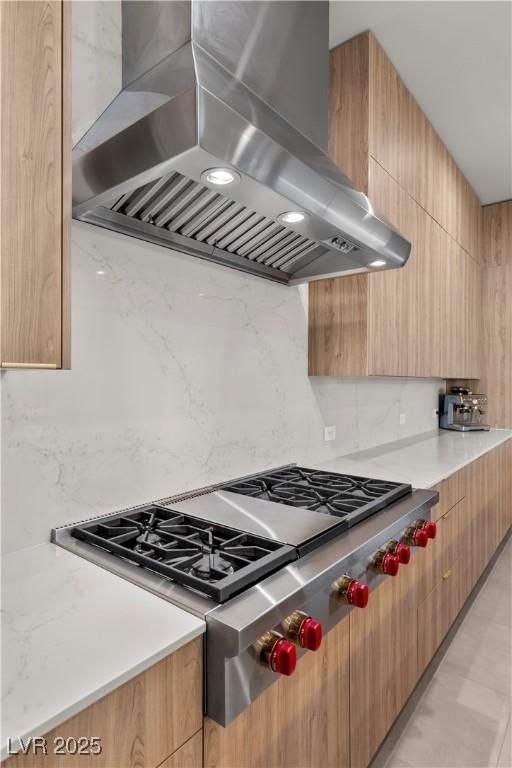 kitchen with modern cabinets, stainless steel gas stovetop, decorative backsplash, island range hood, and light stone countertops