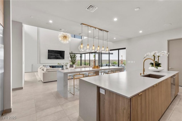 kitchen featuring a large island, visible vents, light countertops, open floor plan, and a sink