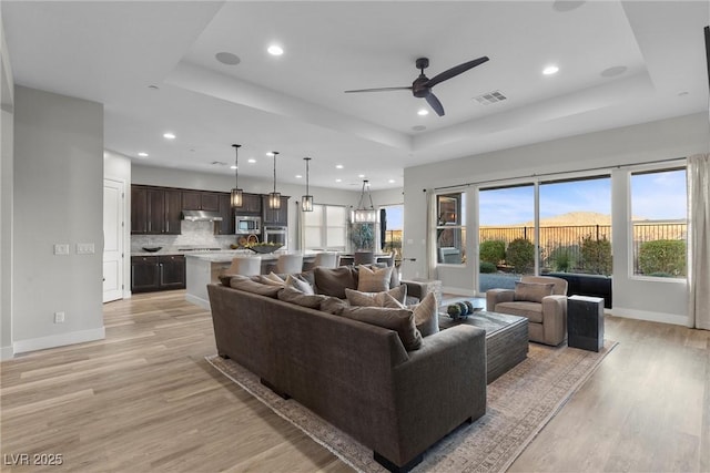 living room with ceiling fan, a raised ceiling, and light hardwood / wood-style floors