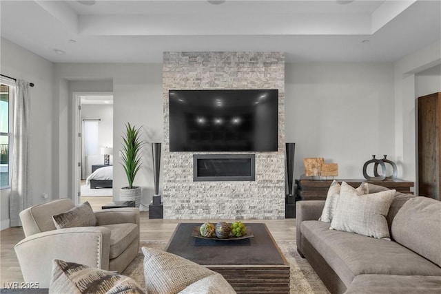 living room featuring a stone fireplace, a raised ceiling, and light wood-type flooring