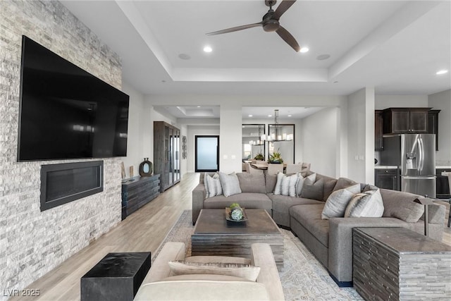 living room with ceiling fan with notable chandelier, a raised ceiling, and light wood-type flooring