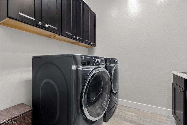 clothes washing area featuring cabinets, light wood-type flooring, and washer and clothes dryer