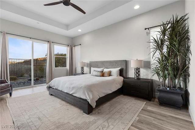 bedroom with access to exterior, a tray ceiling, ceiling fan, and light wood-type flooring