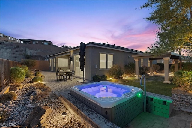 back house at dusk with an outdoor hot tub and a patio area