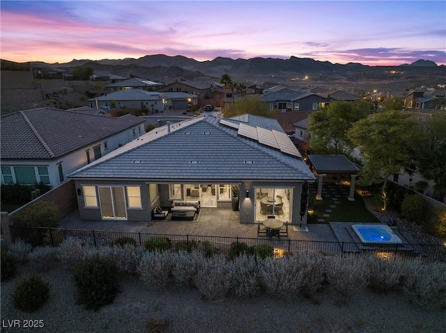 back house at dusk featuring a patio area, solar panels, a mountain view, an outdoor hangout area, and an in ground hot tub