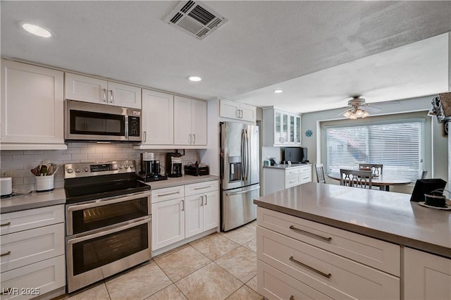 kitchen featuring white cabinetry, light tile patterned floors, appliances with stainless steel finishes, ceiling fan, and decorative backsplash