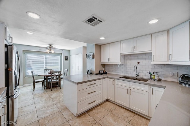 kitchen with white cabinetry, stainless steel fridge, kitchen peninsula, and sink