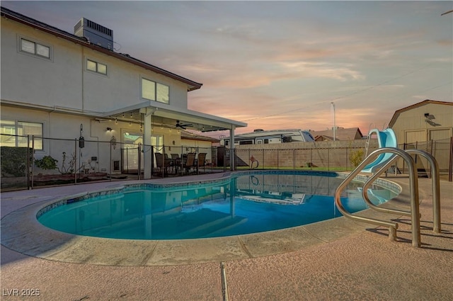 pool at dusk with a patio and a storage unit