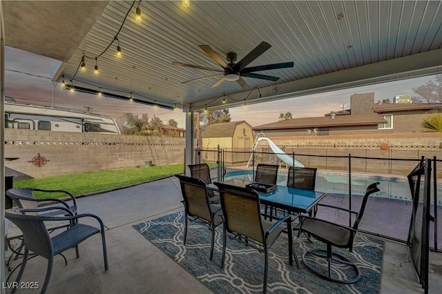 patio terrace at dusk featuring ceiling fan and a storage shed