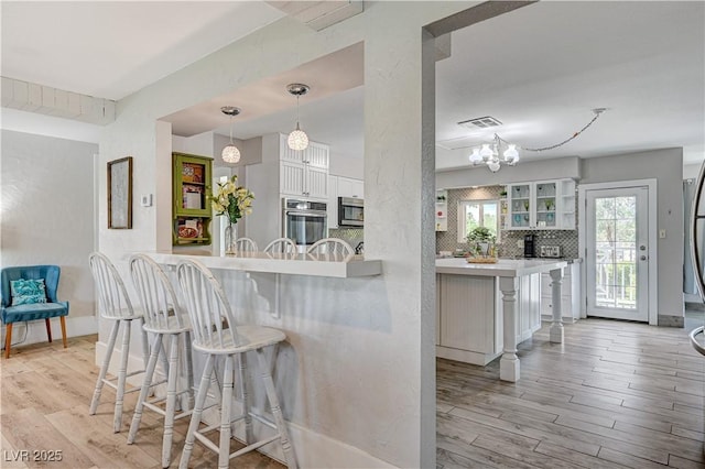 kitchen with a breakfast bar, kitchen peninsula, hanging light fixtures, and white cabinets